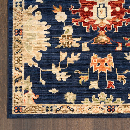 Close-up of a navy blue oriental rug with cream and red geometric motifs and a beige border on dark wood floor.