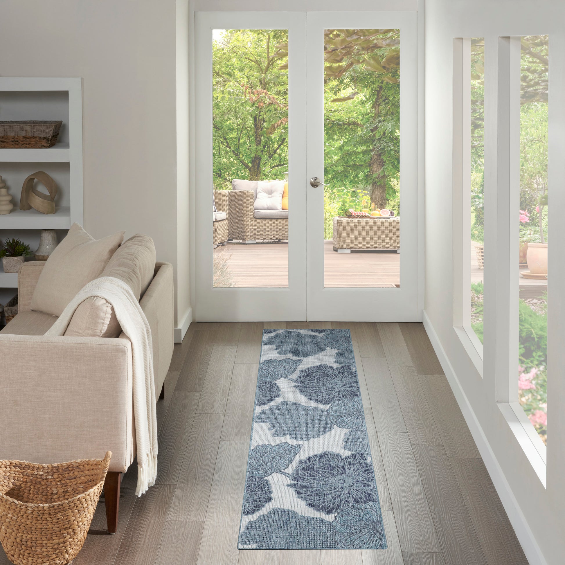 Blue floral runner rug along a light gray wood floor by glass patio doors, beige sofa nearby.