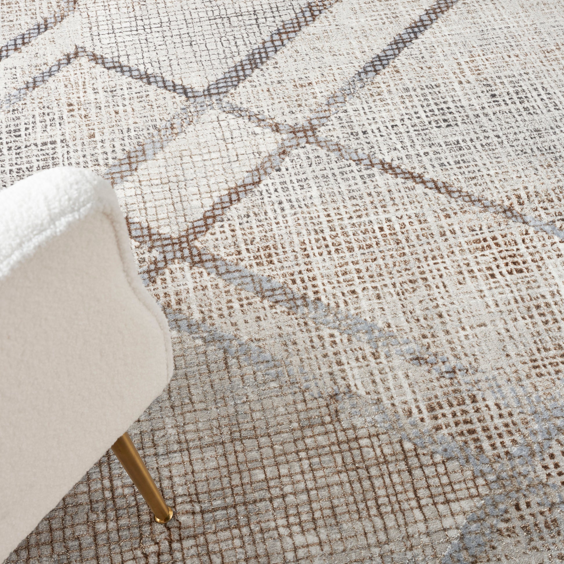 White upholstered chair with slim gold legs on a textured beige geometric rug.