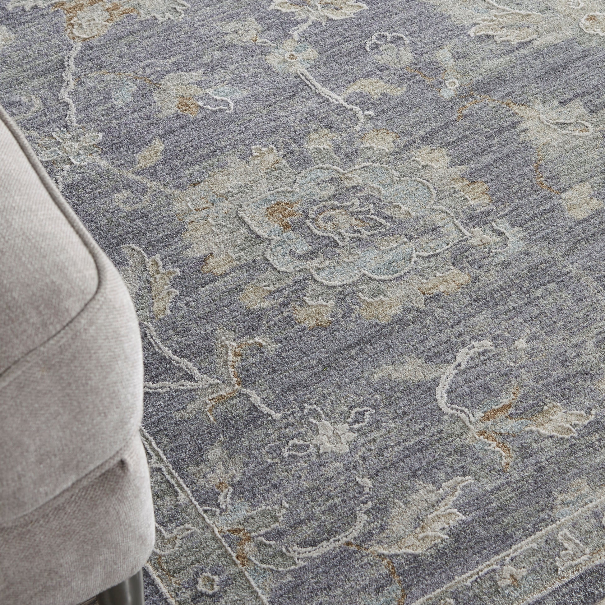 Blue-gray ornate rug with floral medallions; beige upholstered sofa arm visible in corner.