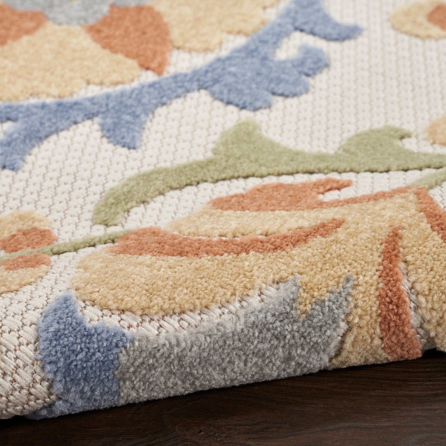 Close-up of a thick-pile area rug with pastel abstract leaf patterns in blue, green and peach on beige.