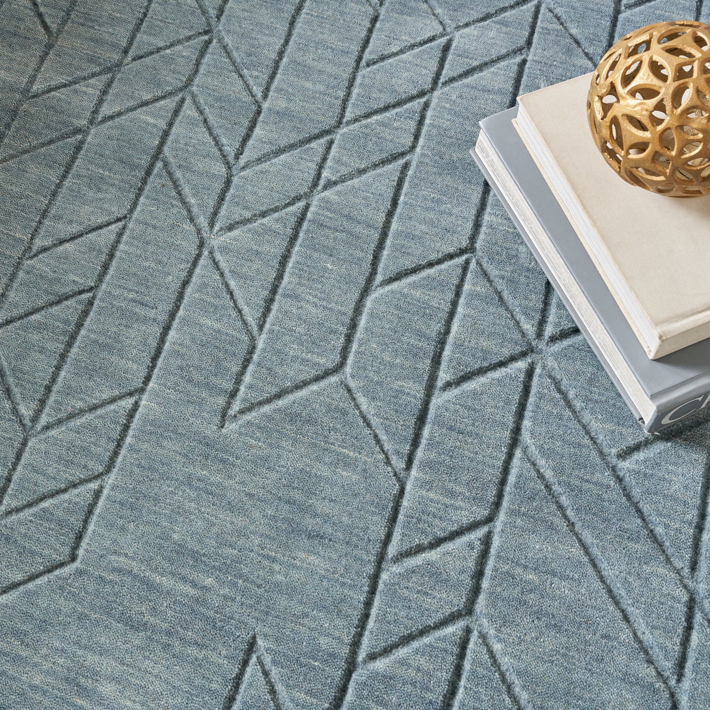 Blue-gray geometric rug with chevron pattern; stack of books topped by a wooden lattice ball.