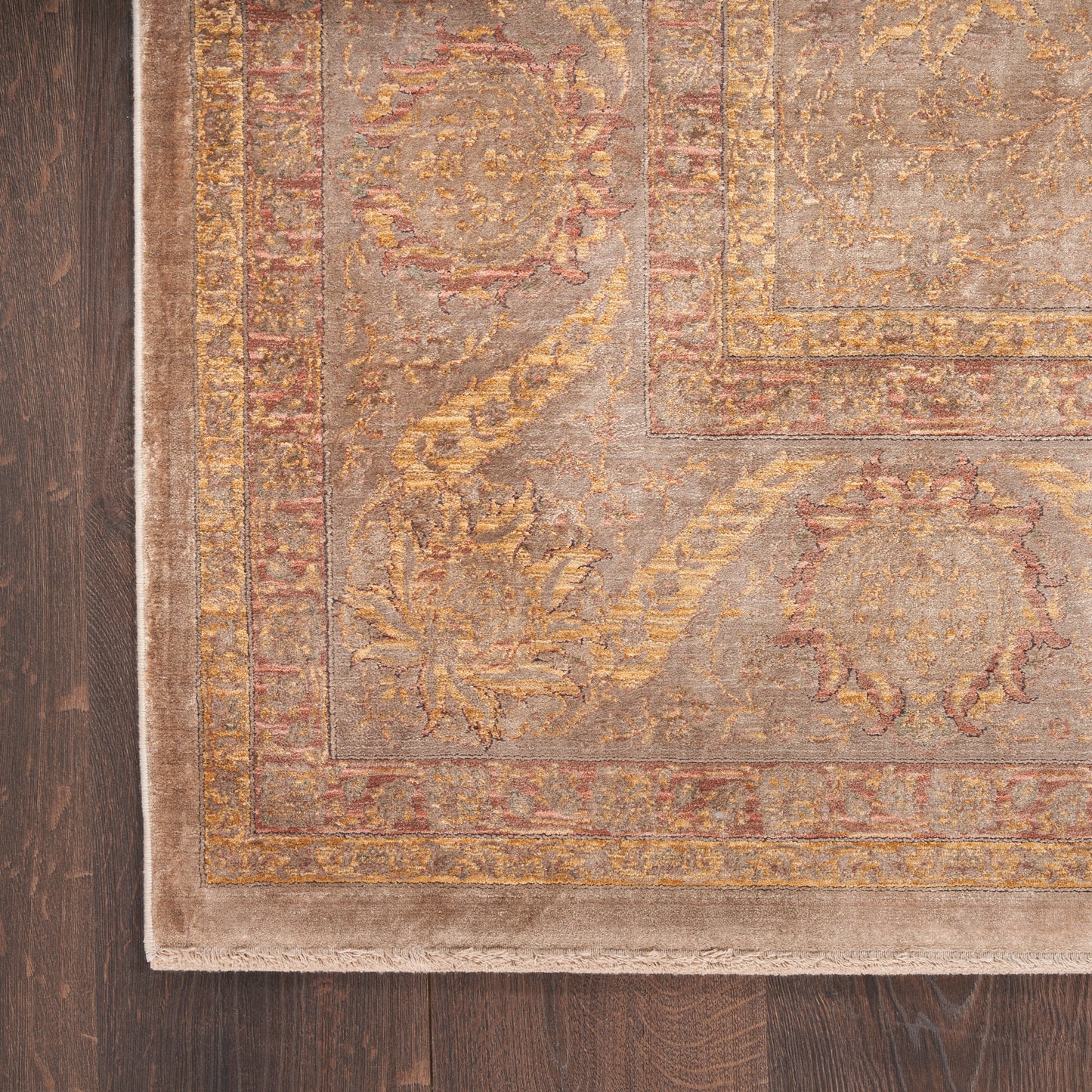 Beige ornamental rug with gold and pink floral pattern, layered borders, on dark hardwood floor.