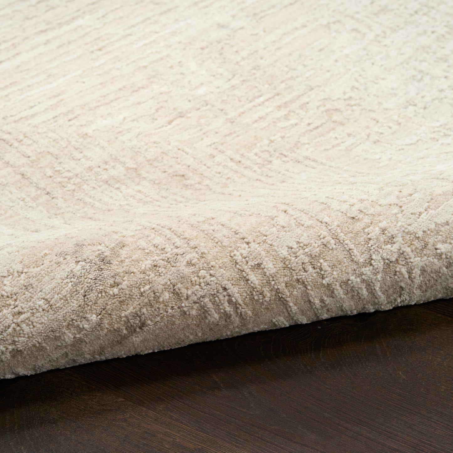 Beige plush area rug with soft pile and subtle pattern, folded edge on dark wood floor.