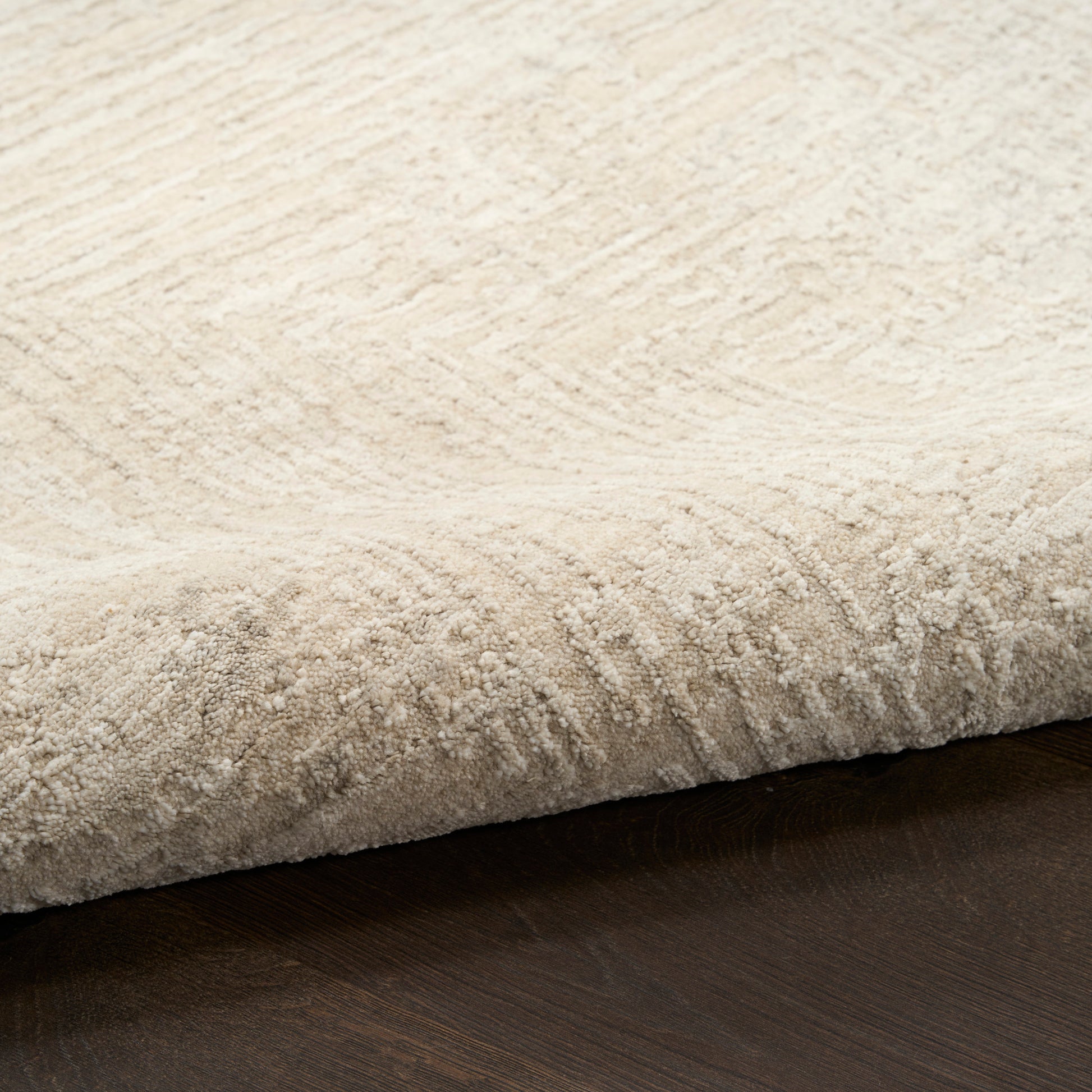 Beige plush area rug with soft pile and subtle pattern, folded edge on dark wood floor.