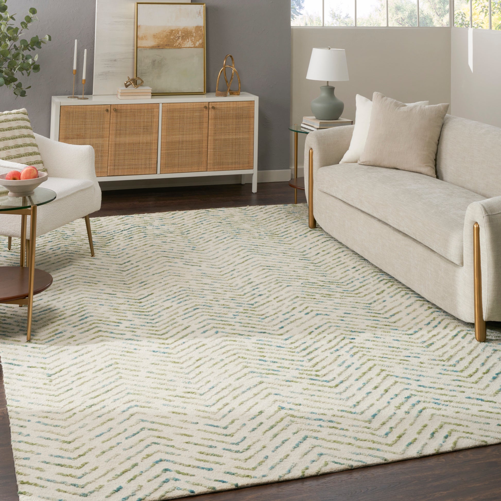 Cozy mid-century living room: beige sofa, woven-cane sideboard, soft blue-green chevron rug, round glass tables, pastel lamp.
