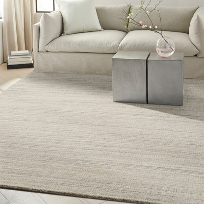 Beige fabric sofa on a light striped rug with two square concrete side tables and a glass vase with branches.