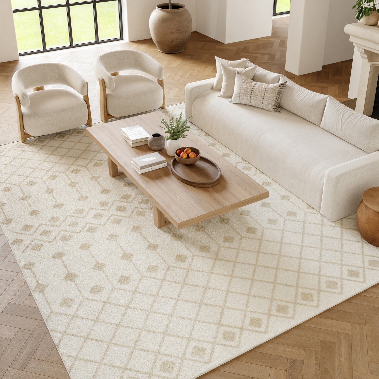 Neutral living room with cream sofa, two rounded cream chairs, light wood coffee table on a beige geometric rug.