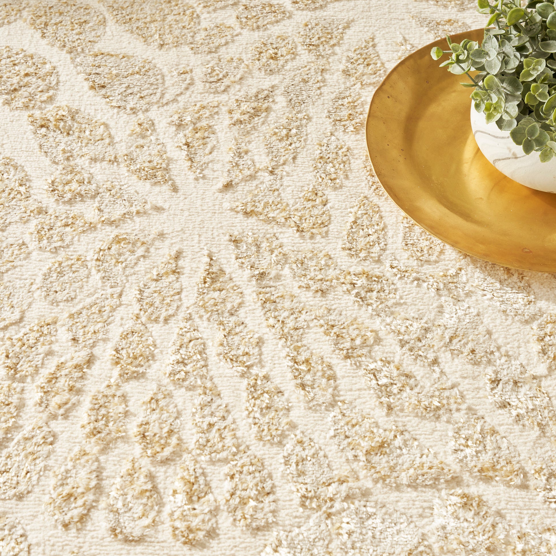 Cream shag rug with a beige sunburst pattern; plush texture, gold tray and potted plant in top-right.