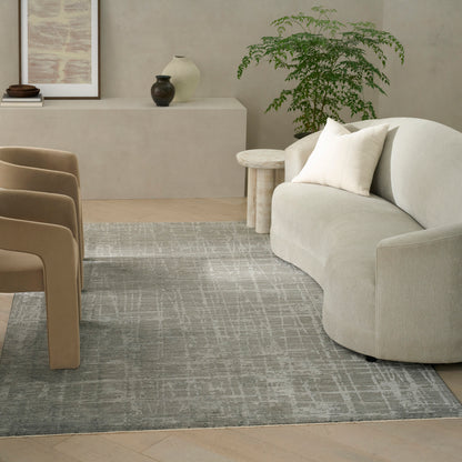 Neutral living room with curved beige sofa, white pillow, tan chairs, round side table, light gray patterned rug, greenery.
