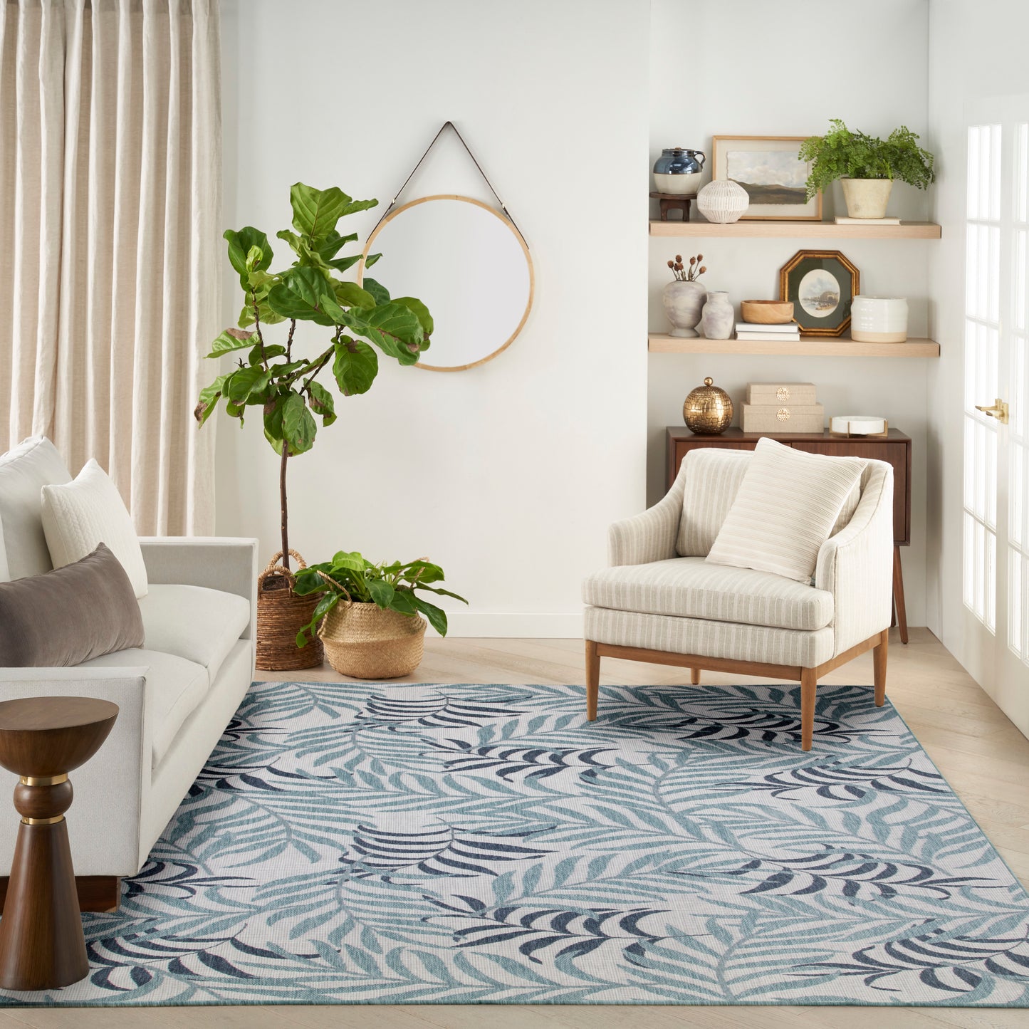 Cozy living room with beige striped armchair, light sofa, blue leaf-pattern rug, and wood shelves with plants and decor.
