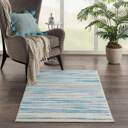 Blue striped area rug in a cozy living room with a grey armchair, blue tassel pillow, beige throw, and large potted plant.