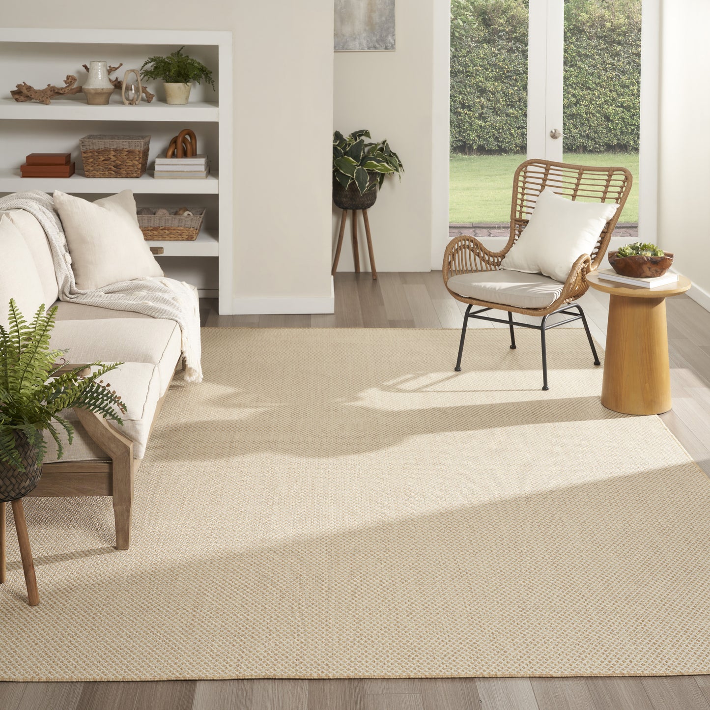 Bright living room with beige woven rug (9' x 12'), light sofa, rattan chair, white cushion, wooden side table, and doors to the garden.