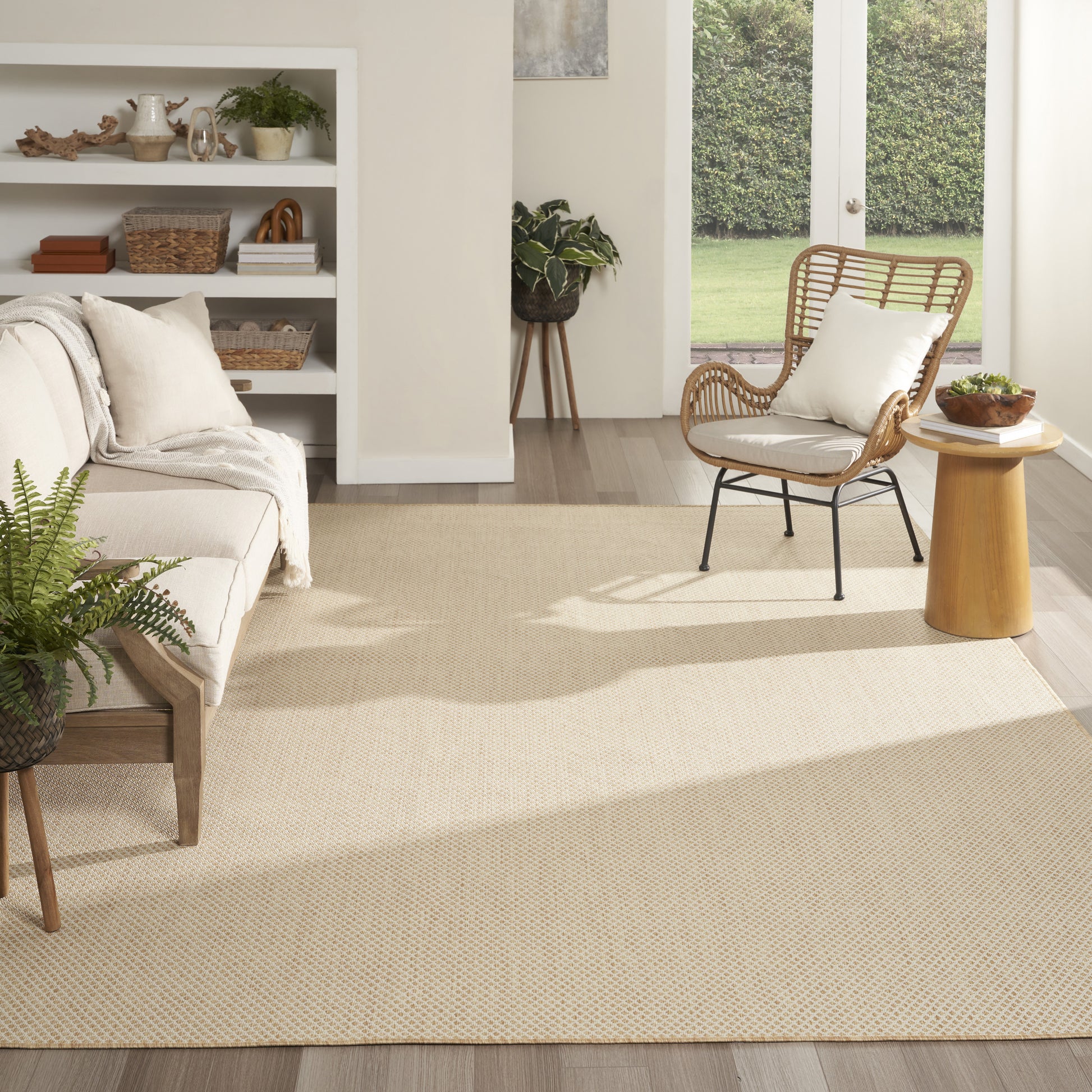 Bright living room with beige woven rug (9' x 12'), light sofa, rattan chair, white cushion, wooden side table, and doors to the garden.