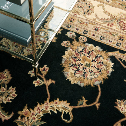 Dark ornate rug with cream and beige floral medallions and vines; glass & brass shelf with blue books nearby.