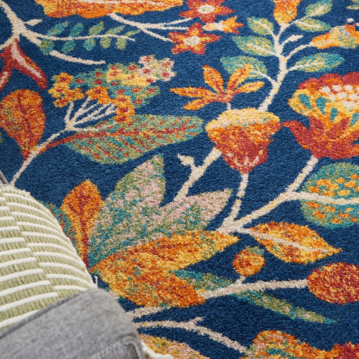 Colorful floral rug with blue background, orange and yellow blooms, green leaves; corner of wicker chair visible.