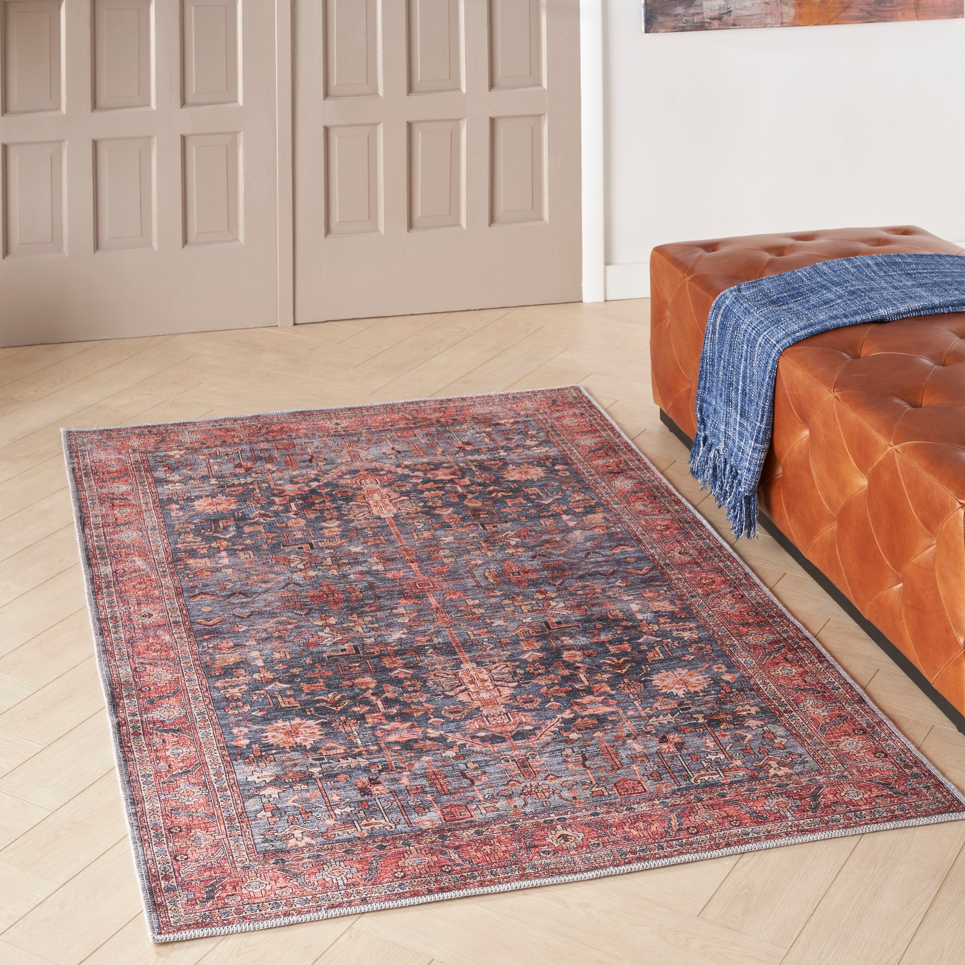 Vintage oriental rug with red border and dark blue center, placed beside an orange tufted sofa with a blue throw.