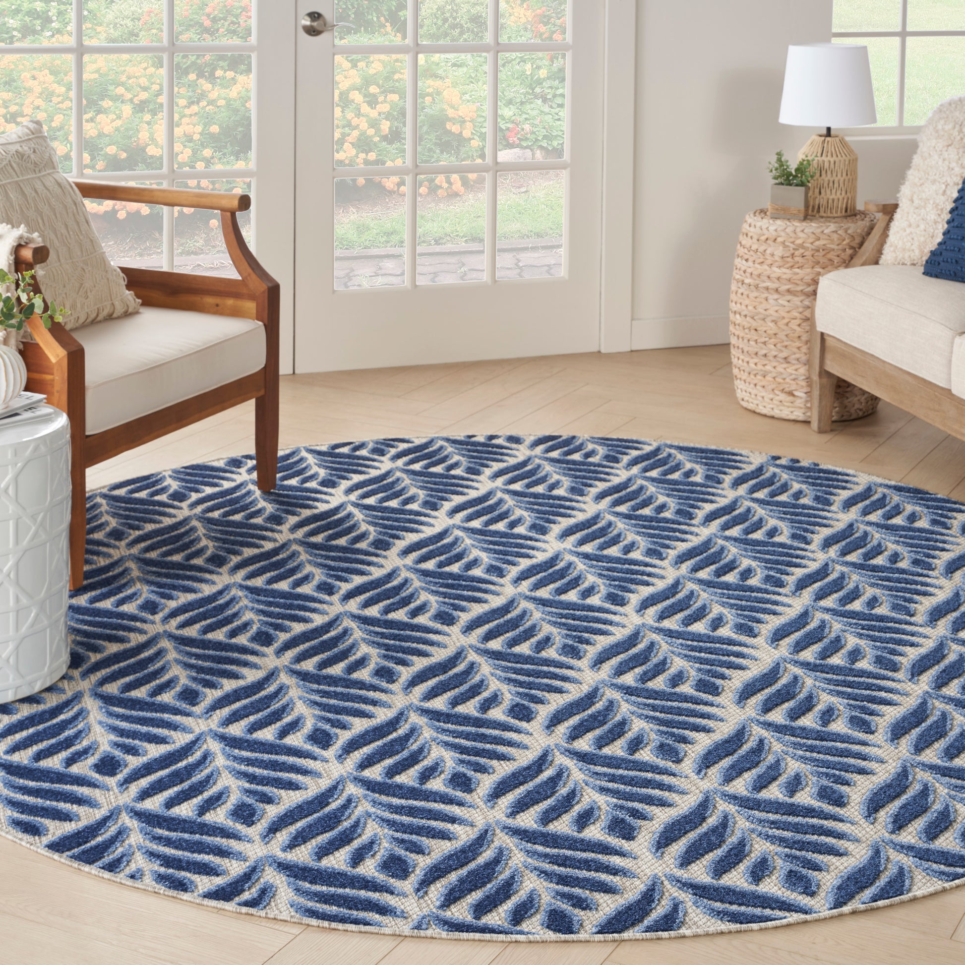 Round blue and ivory rug with leaf-like wave pattern in a bright living room beside wicker side tables.
