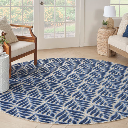 Round blue and ivory rug with leaf-like wave pattern in a bright living room beside wicker side tables.