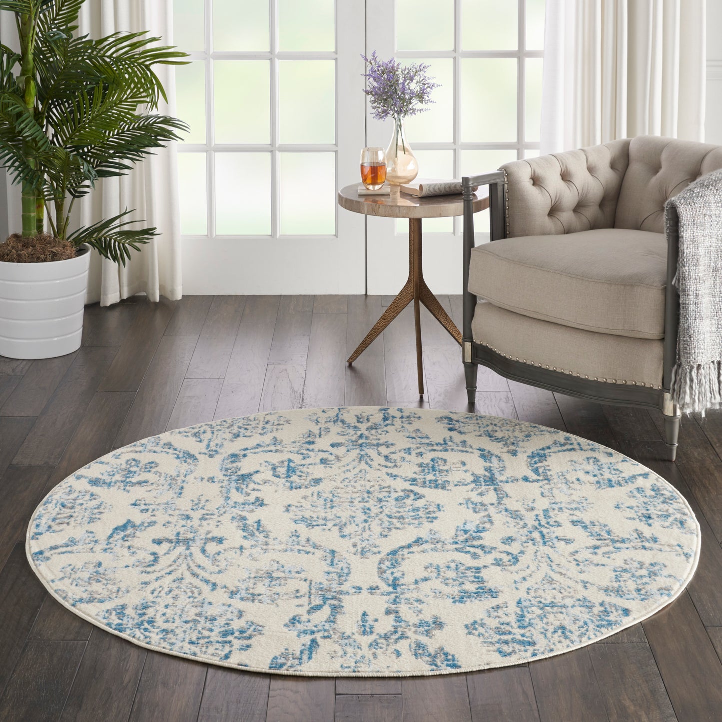 Round cream rug with blue damask pattern in a modern living room beside a tufted beige chair and a wooden side table.