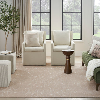 Cozy living room with two beige armchairs, round wooden side table, green sofa, pale patterned rug, tall plant, large windows.