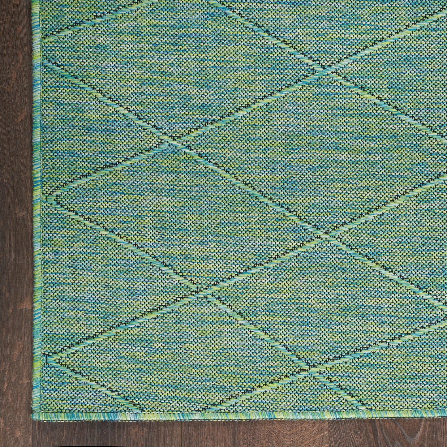 Teal-green woven rug with a diamond lattice pattern and teal border, textured surface on dark wood floor.
