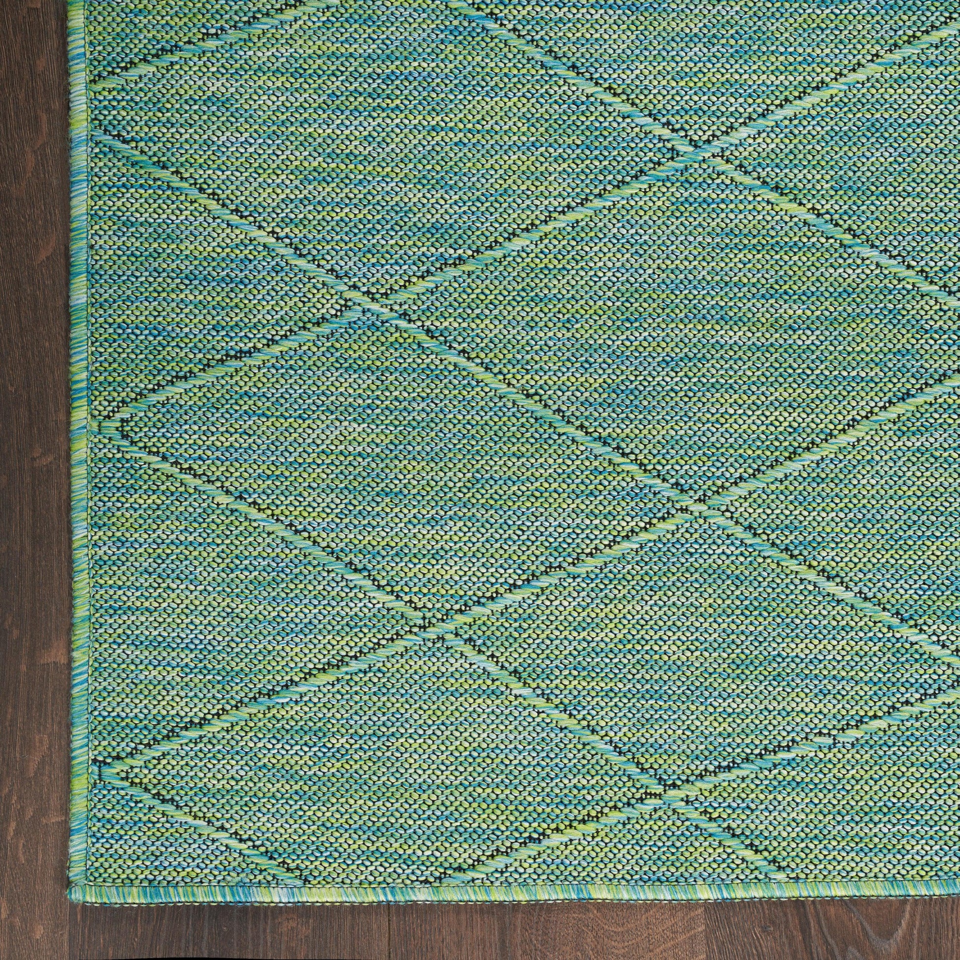 Teal-green woven rug with a diamond lattice pattern and teal border, textured surface on dark wood floor.