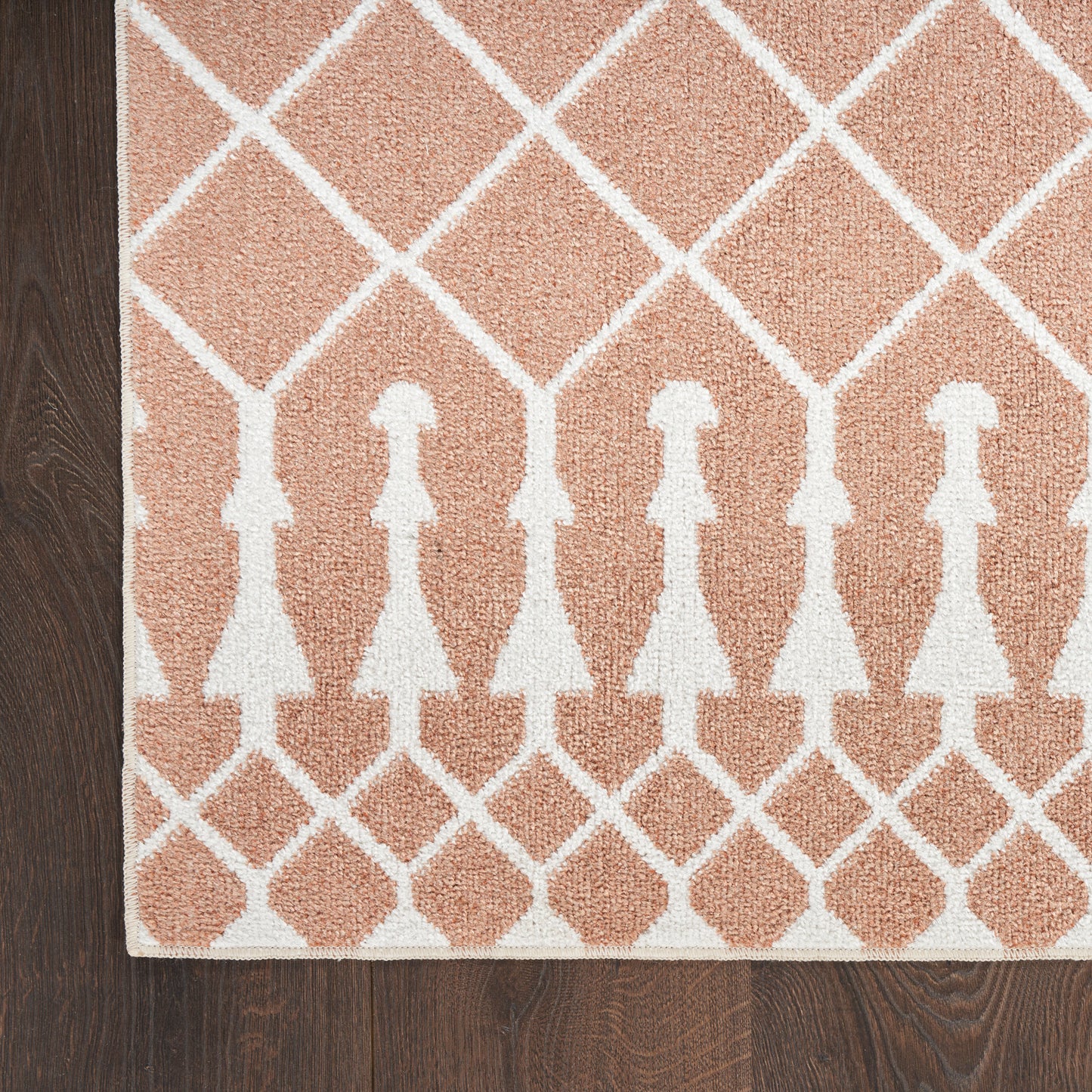 Peach area rug with white lattice diamonds and repeating dress-shaped silhouettes, edged border on dark wood floor.