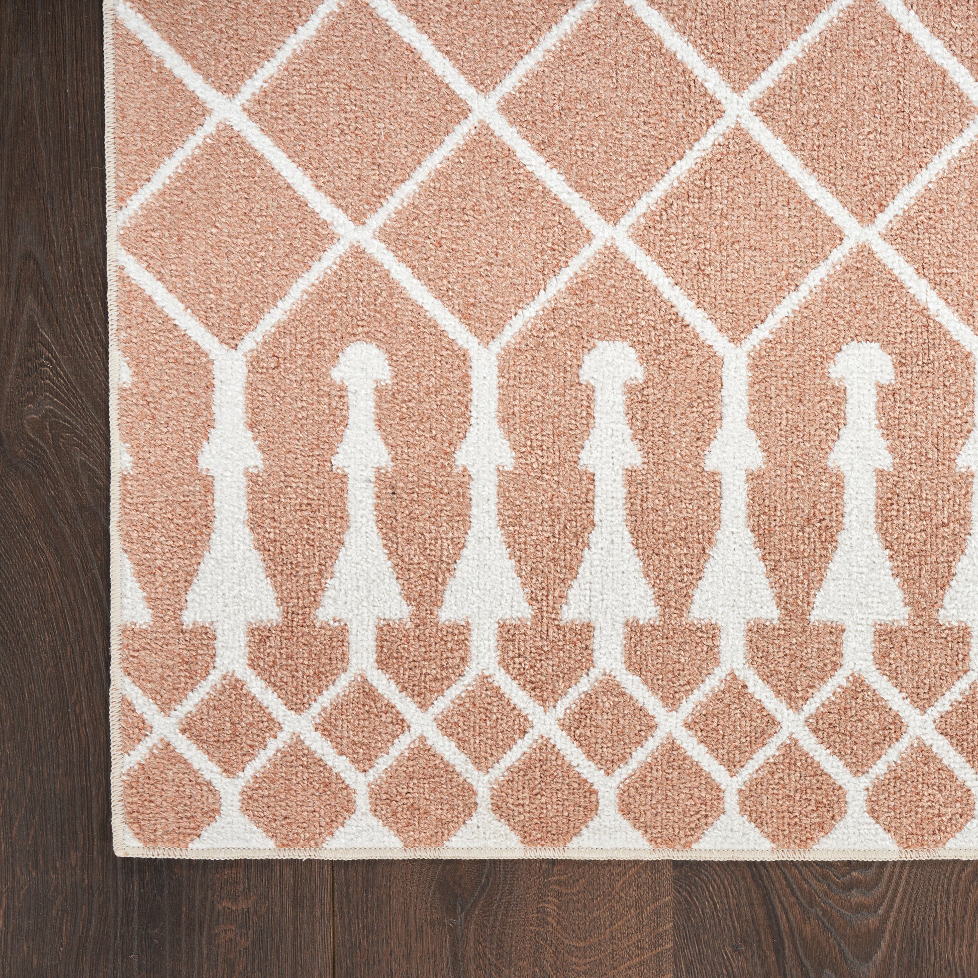 Peach area rug with white lattice diamonds and repeating dress-shaped silhouettes, edged border on dark wood floor.