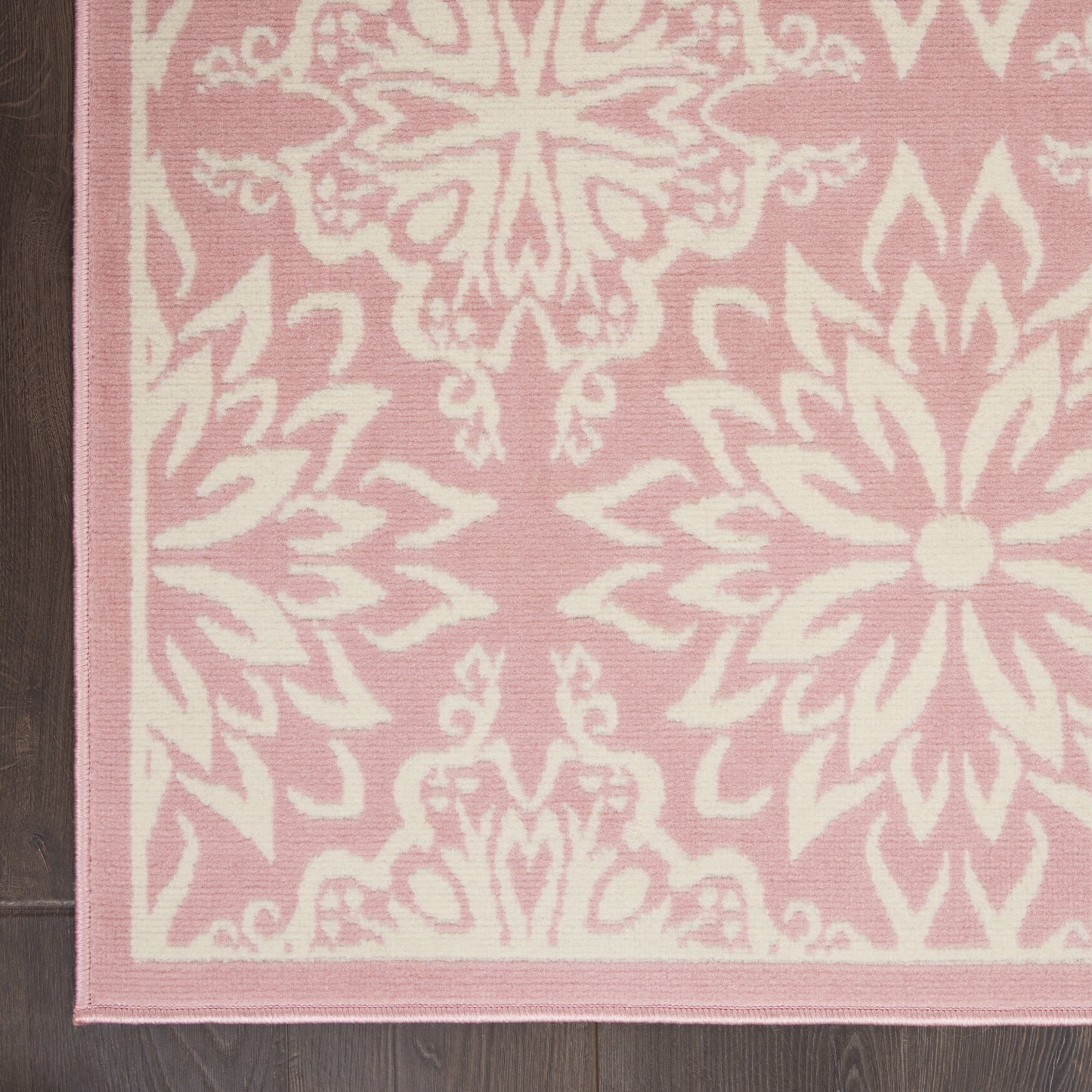 Pink area rug with white damask floral pattern and pale pink border on dark wood floor.