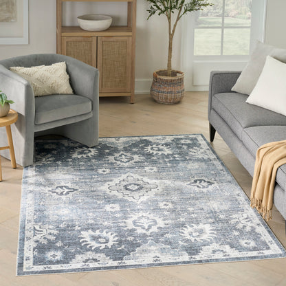 Blue-gray distressed area rug with white floral medallions in a bright living room with a gray sofa and armchair