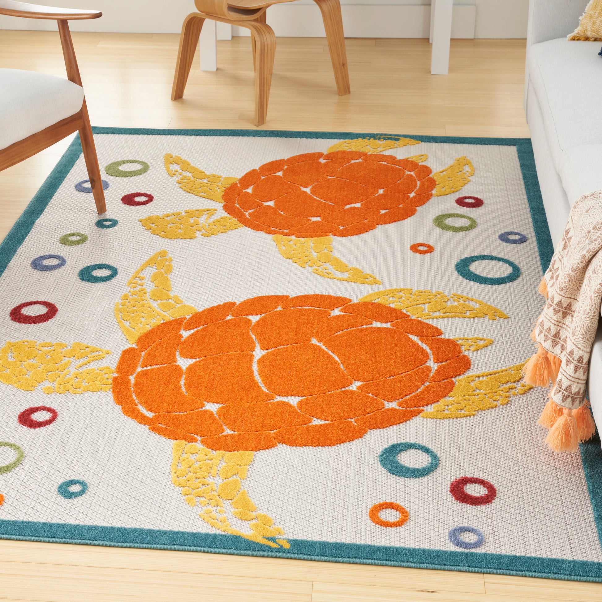 Two orange sea turtles with yellow fins on a white rug with teal border and multicolored circles, in a living room.