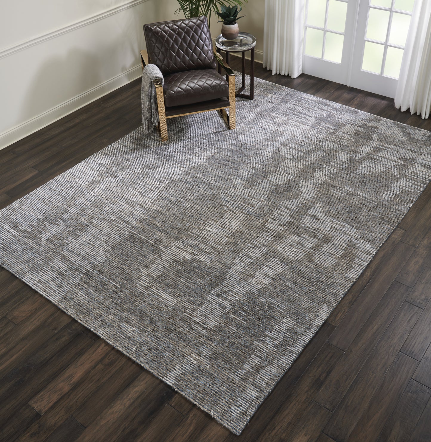 Large rectangular gray textured rug on dark wood floor; brown quilted leather armchair in a modern cozy living space.