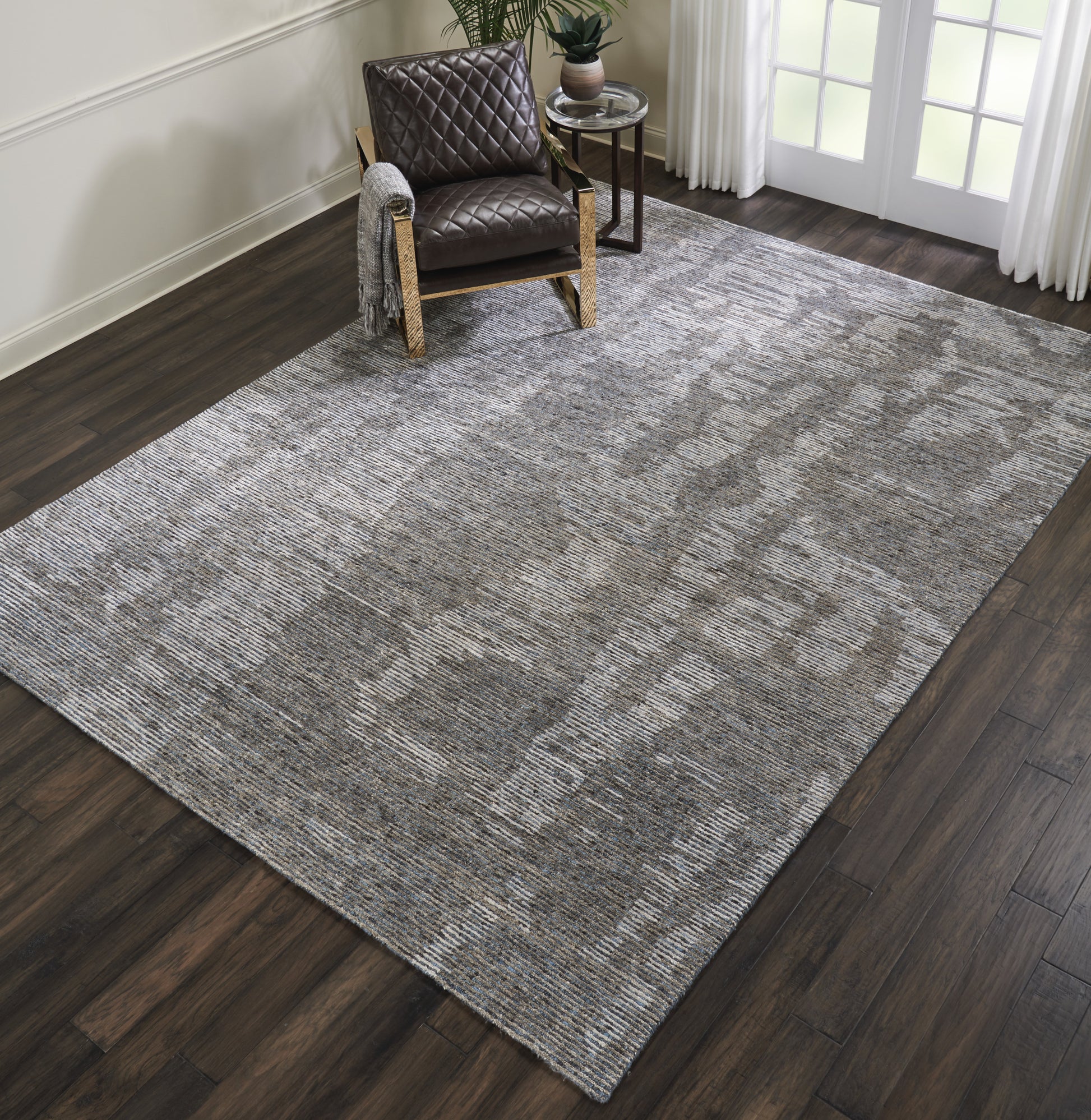 Large rectangular gray textured rug on dark wood floor; brown quilted leather armchair in a modern cozy living space.