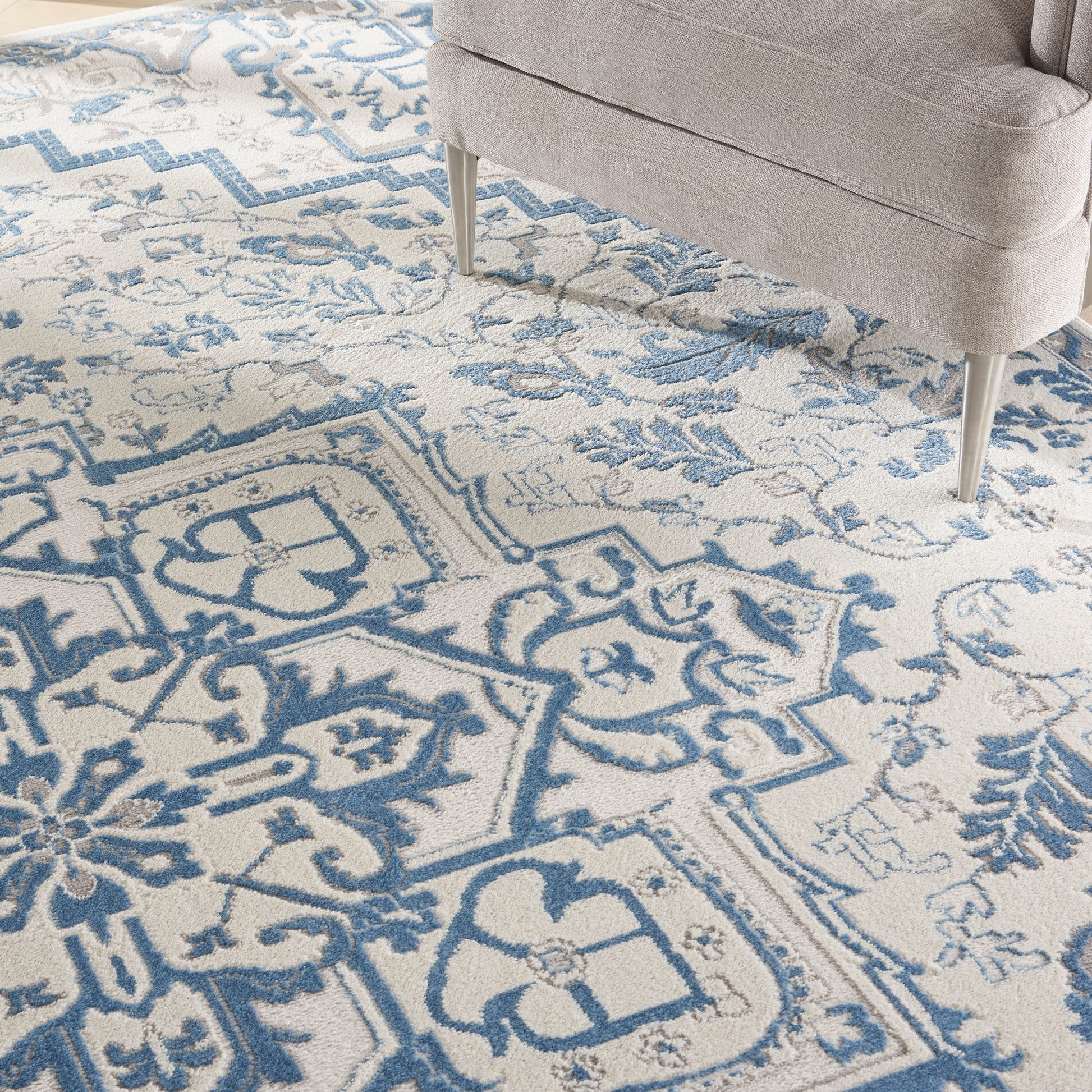 Blue and ivory geometric floral area rug with medallion motifs under a beige upholstered chair.