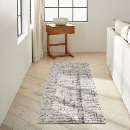 Warm wood console table with a drawer and slender legs, cream ceramic bowl on top, in a bright living room with a gray abstract runner rug.