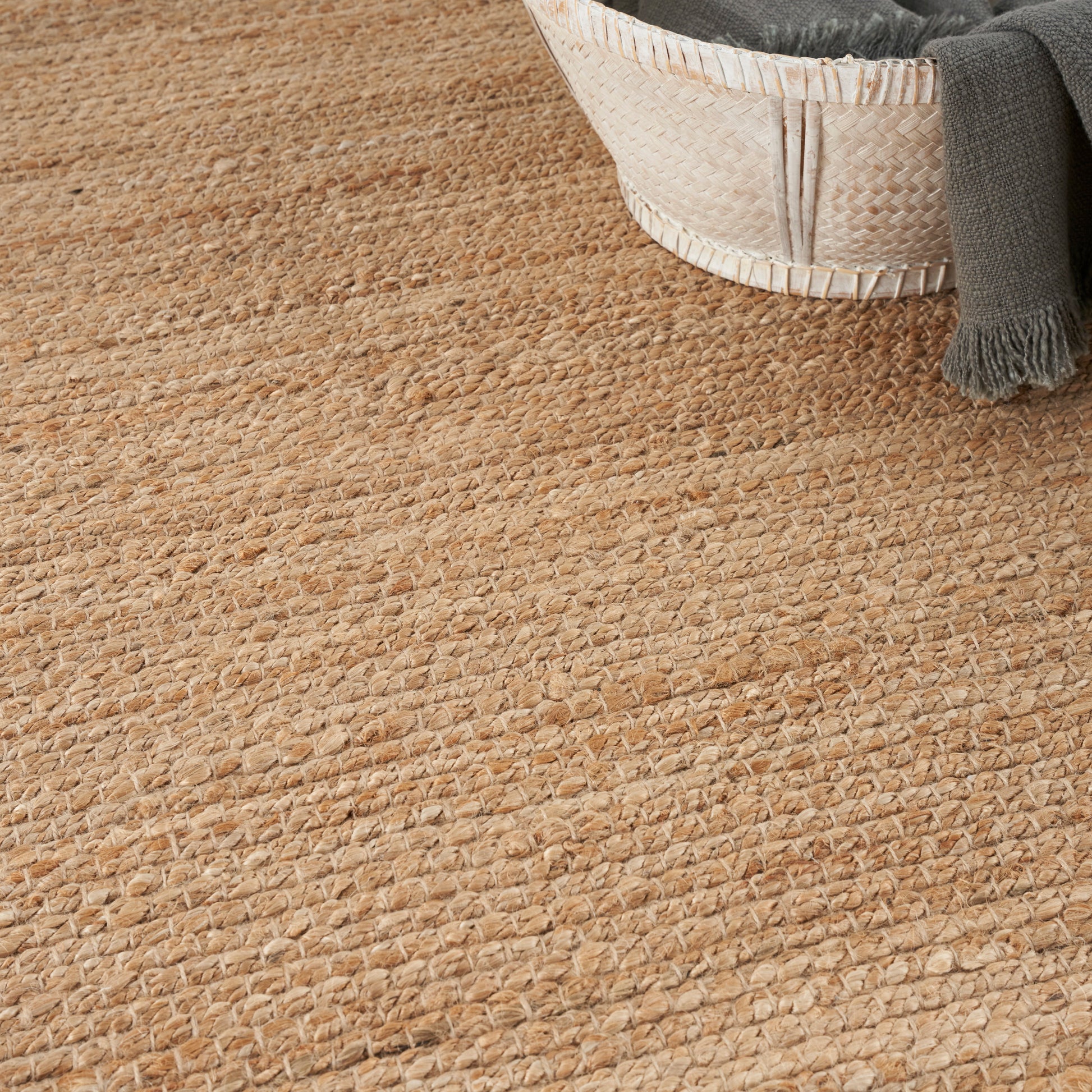 Natural jute rug with chunky woven texture; light basket and gray throw at edge.