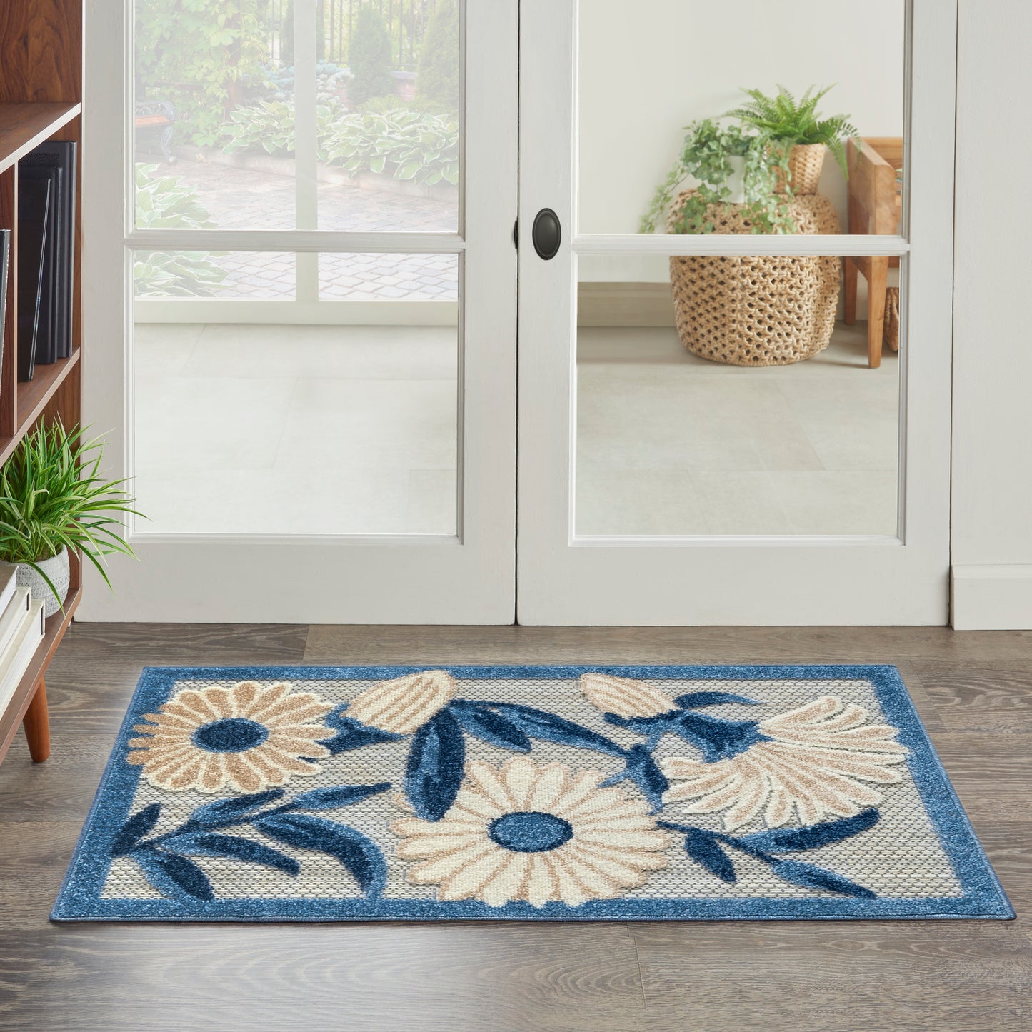 Rectangular door mat with blue border, cream daisies and dark blue leaves on a beige woven background.