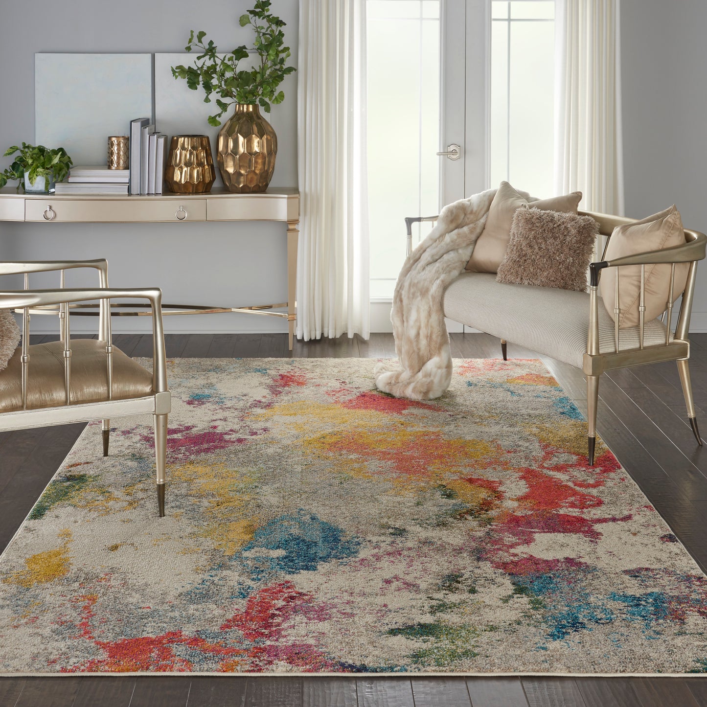 Gold metal-framed chairs, cream sofa, plush fur throw, and a multicolor abstract rug with red, yellow, teal accents.