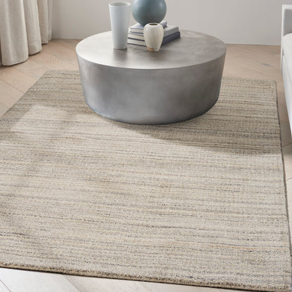 Round gray concrete coffee table with vases and books on top on a beige woven rug in a modern living room.