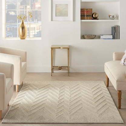 Cream living room with a light chevron rug, beige sofas, a gold vase on the window sill, and white built-in shelves with decor.