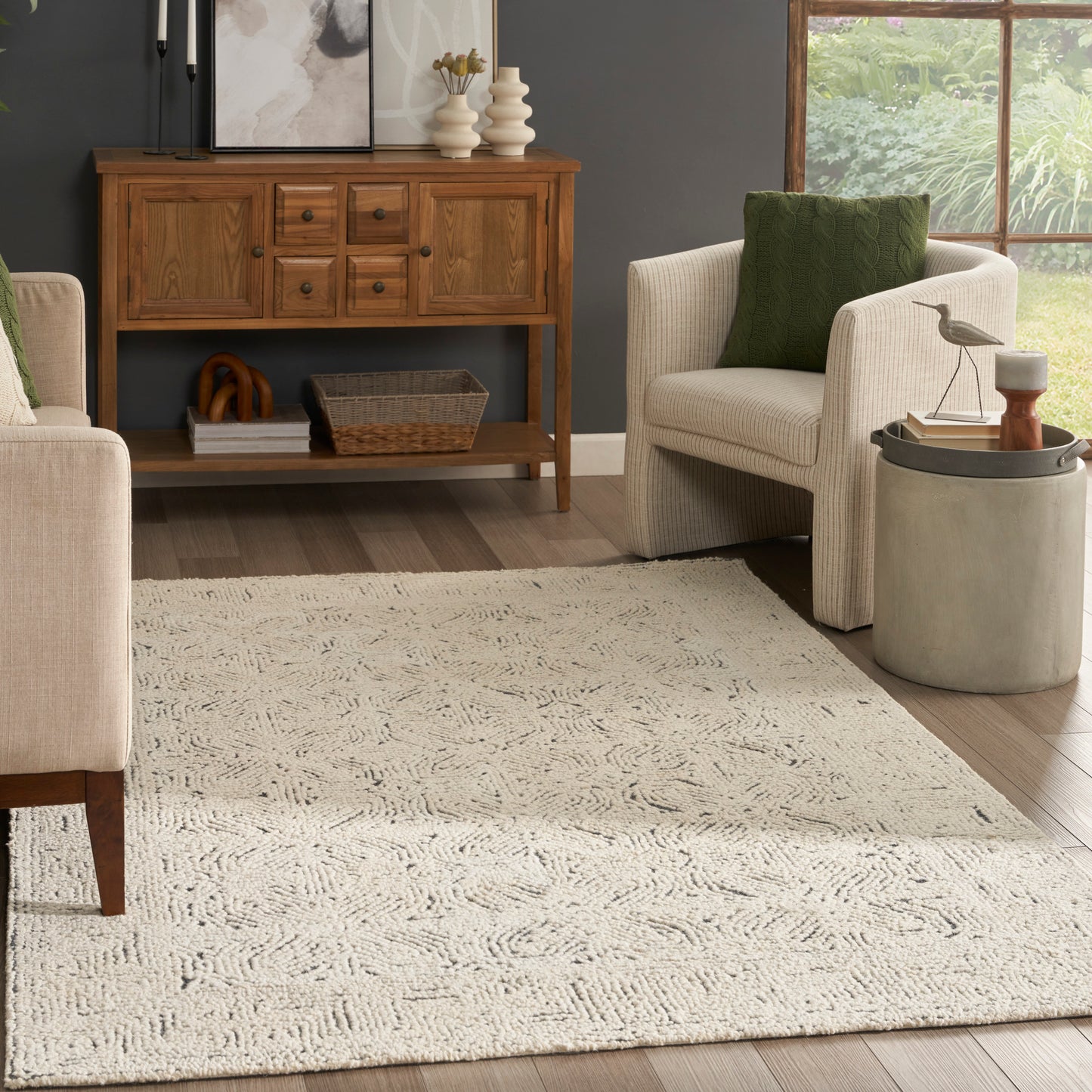 Beige upholstered chairs with wooden console, cream textured rug, green pillow, and metal drum side table with bird statue.
