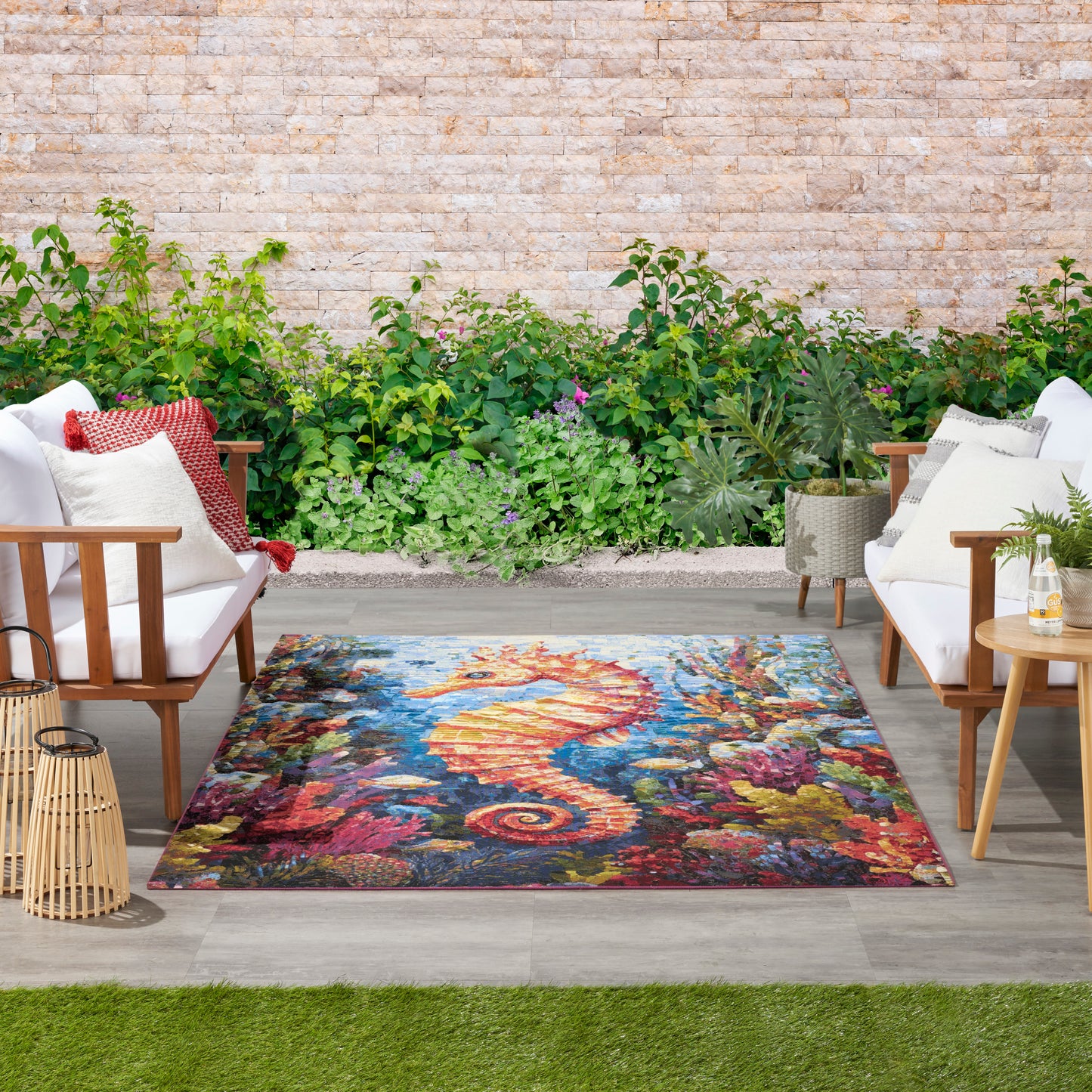 Outdoor patio lounge with white cushioned wooden chairs, vibrant seahorse rug, lush greenery backdrop and lanterns.