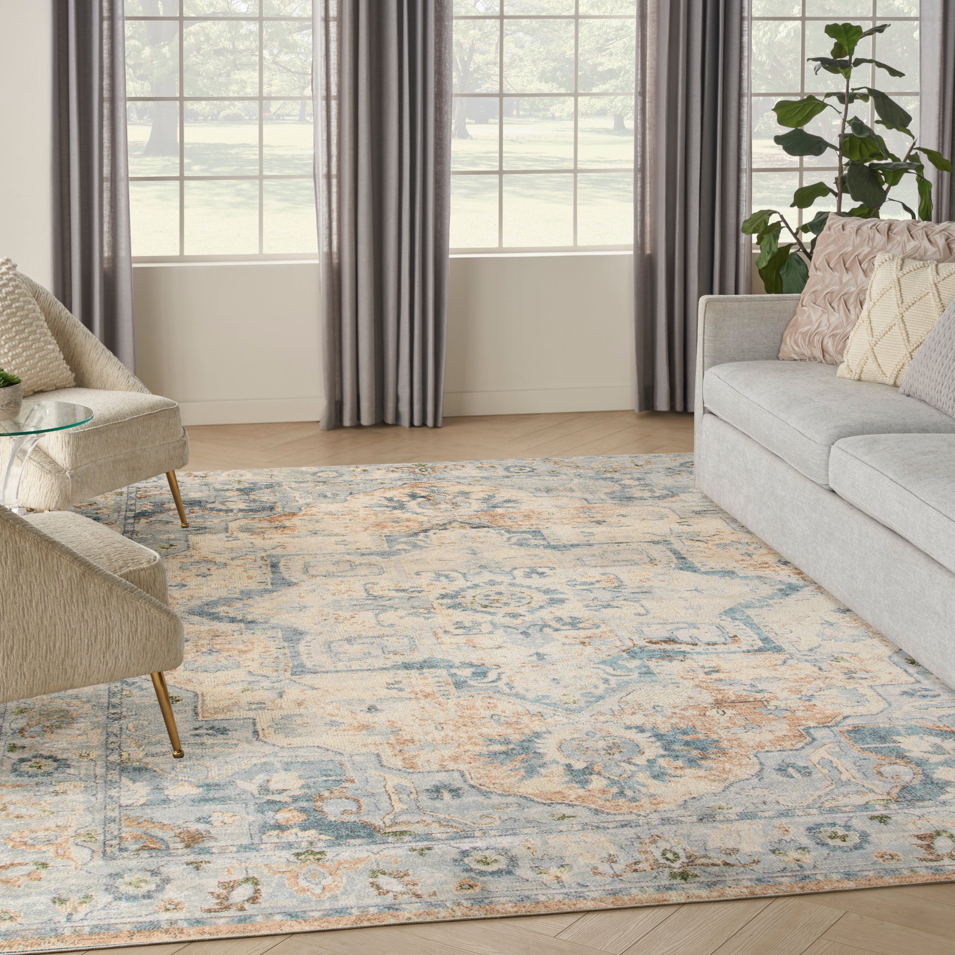 Living room with a large pastel patterned area rug in blue, cream and peach, beige chairs, gray sofa, and gray curtains.