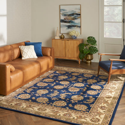 Tan leather sofa, blue cushions, navy floral rug with beige border, mid-century wood sideboard, blue armchair, plant.
