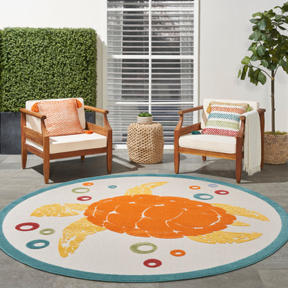 Outdoor two wooden-armchair seating with white cushions and colorful pillows; round teal-bordered rug with an orange crab.