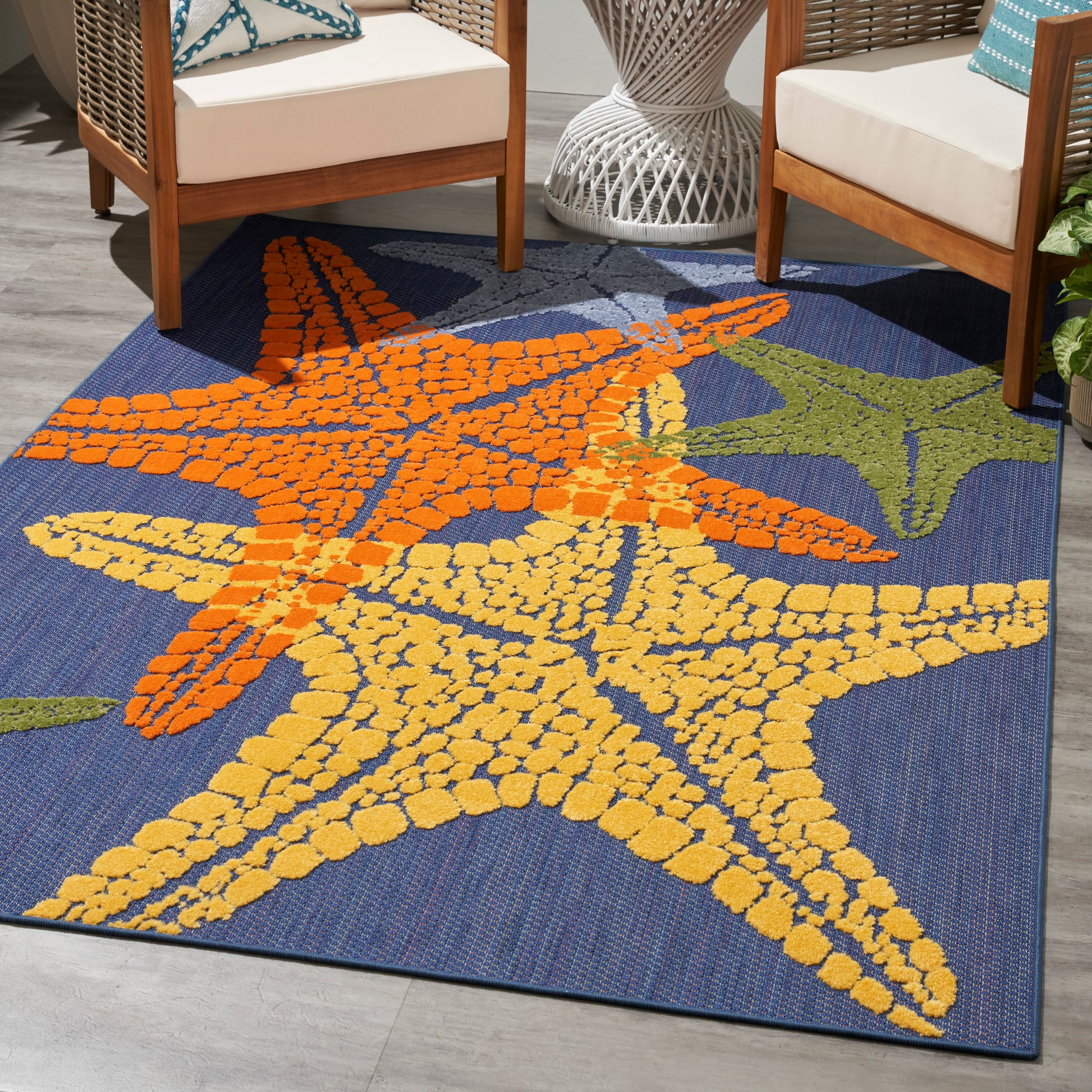 Outdoor coastal rug with large orange and yellow starfish on navy blue, woven texture for patio seating.