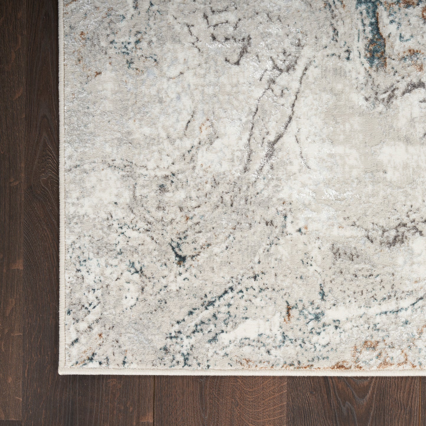 Light gray abstract area rug with blue-gray veining and a pale border on dark wood floor.