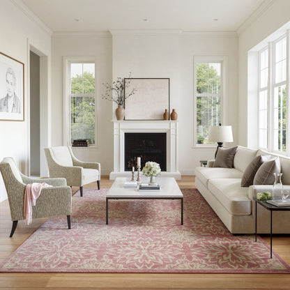 Bright living room with white walls, pink floral rug, beige sofa, two patterned armchairs, glass coffee table, and fireplace.
