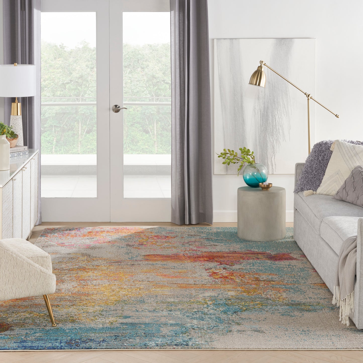Bright living room with a vibrant multicolor area rug, beige sofa, brass floor lamp, glass vase on a pedestal, and doors.